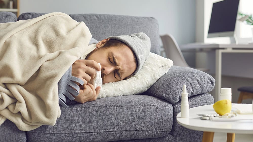 Close up of a sick man with a runny nose with a napkin in his hands lying on the couch